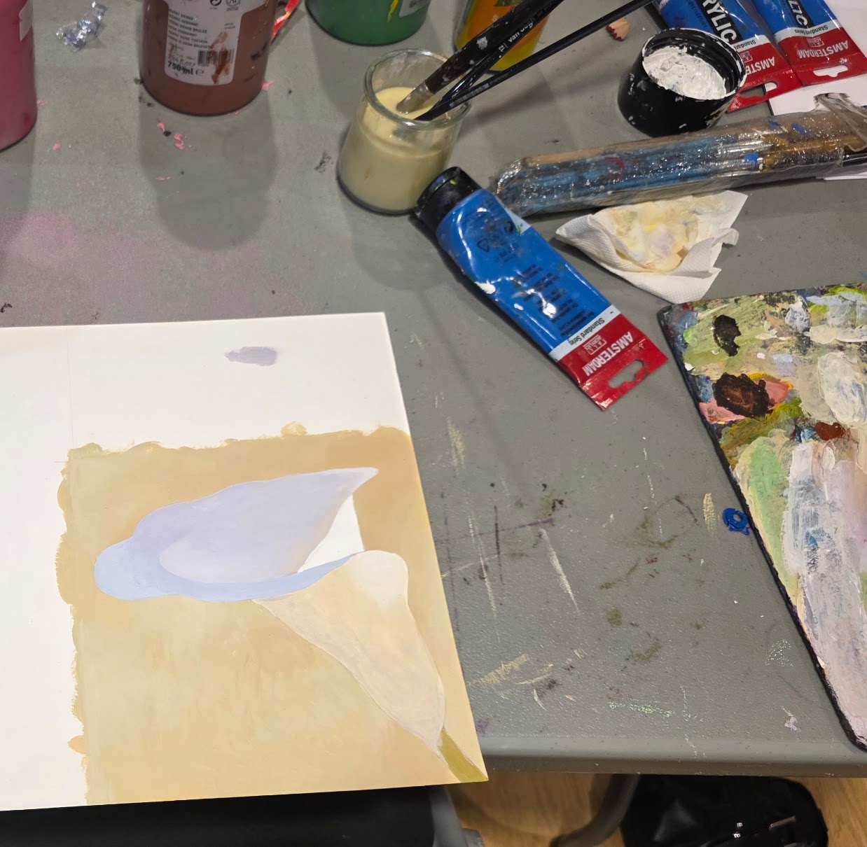 Work in progress: first layers of a calla lily painting by ArtY on the studio table, surrounded by acrylic paint tubes, brushes and palette